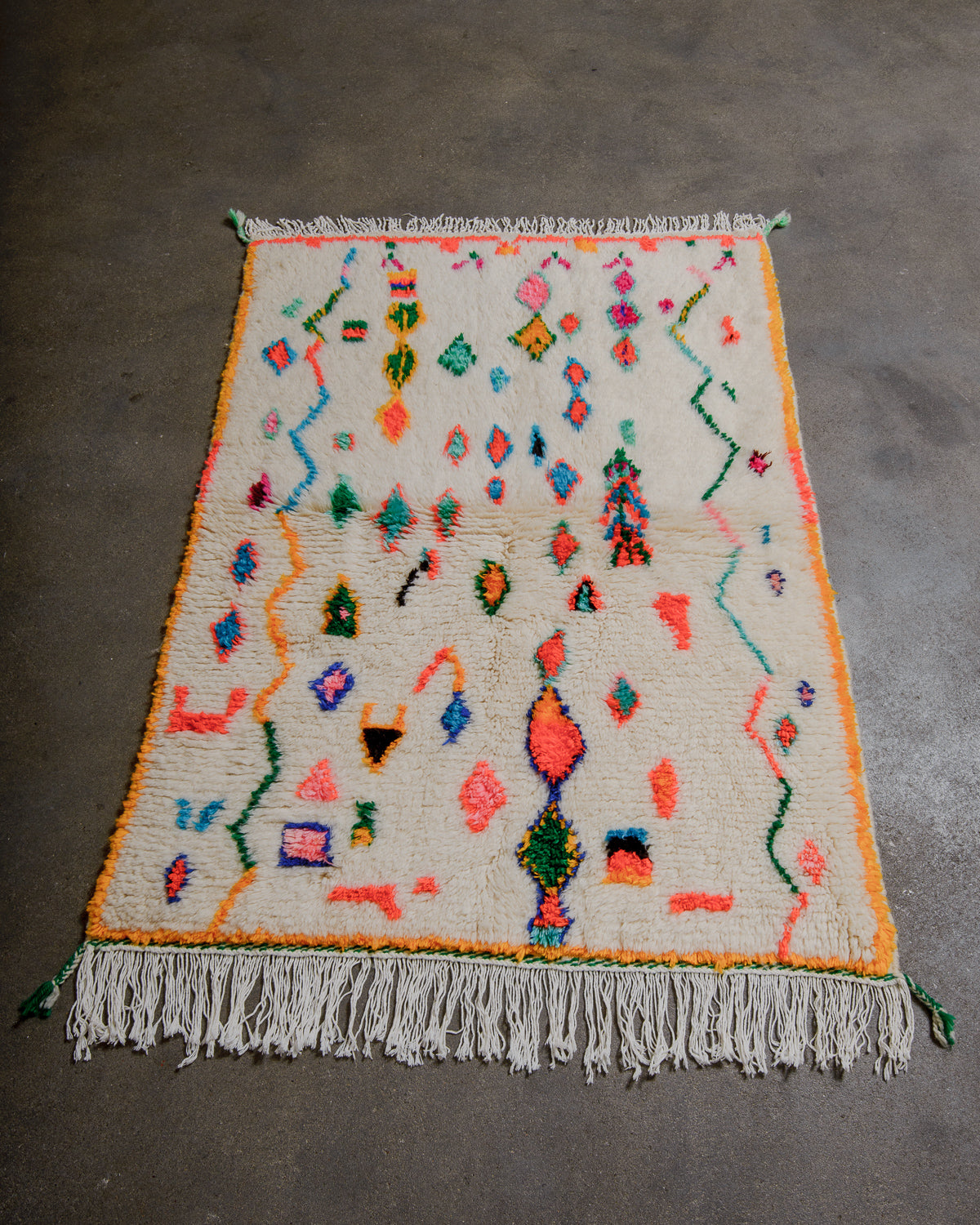Colorful geometric azilal patterned rug with fringe on a gray floor